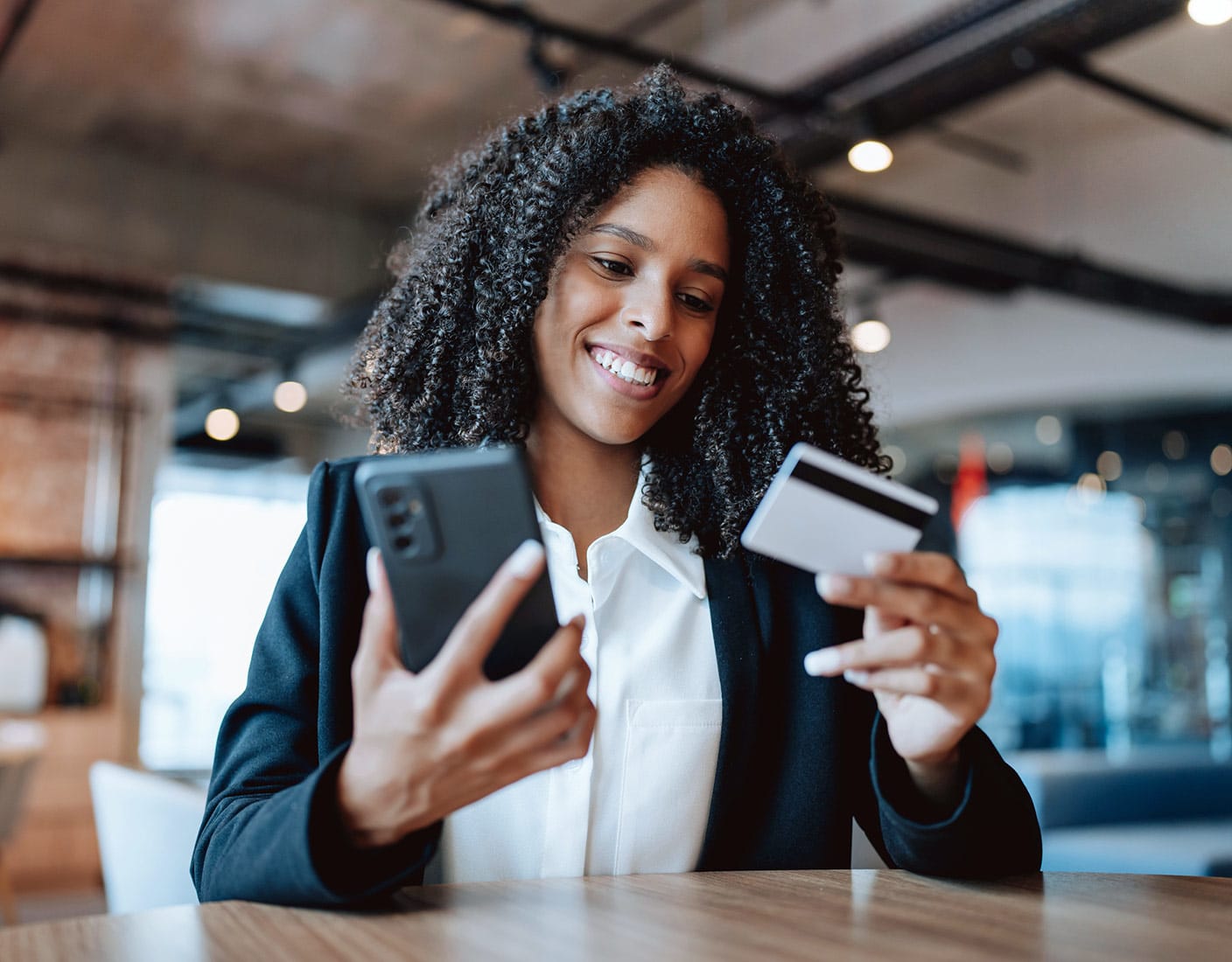 A woman with curly hair is seen holding a credit card and looking at her phone, indicating a banking activity.